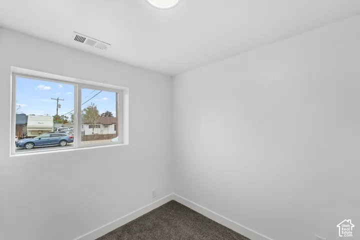 Neutral interior space featuring white-painted walls, grey carpeting, and a sliding window with white trim
