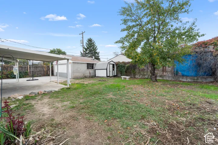 Backyard featuring a concrete-pad carport, detached garage, storage shed, perimeter wood fencing, and mature trees