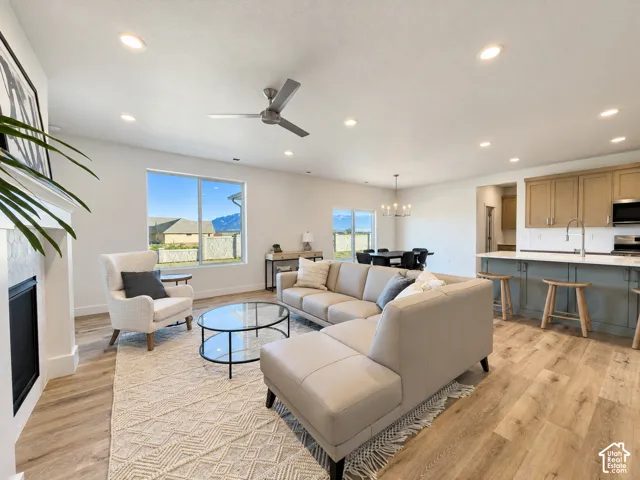 Open-concept living space featuring wood-finish flooring, recessed lighting, a modern ceiling fan, a fireplace with a geometric-patterned surround, and an island kitchen with natural wood-tone cabinetry