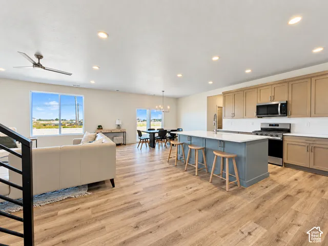 Open-concept interior featuring wood-finish flooring, a kitchen island with a light-colored countertop, shaker-style cabinetry, recessed ceiling lighting, and a modern ceiling fan
