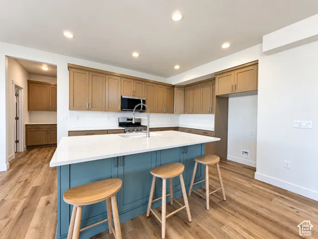 Kitchen featuring wood-finish cabinetry, a central island with a contrasting blue finish, stone-surface countertops, wood-finish flooring, and recessed ceiling lighting