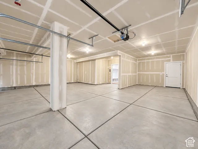 Spacious multi-car garage featuring finished drywall, concrete flooring with expansion joints, automatic garage door openers, and a dedicated entry door