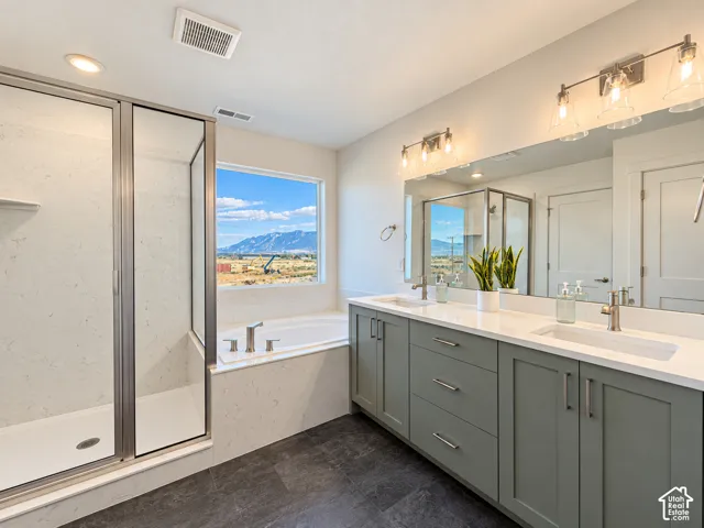 Dual vanity with solid surface countertops, walk-in glass-enclosed shower, soaking tub, slate-finish floor tile, and mountain landscape imagery