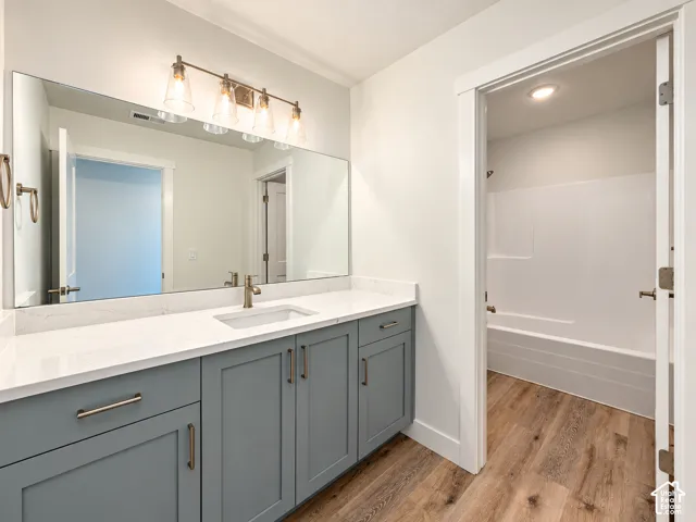 Bathroom featuring a vanity with blue shaker-style cabinetry, white solid-surface countertop, rectangular undermount sink, and four-light metal fixture