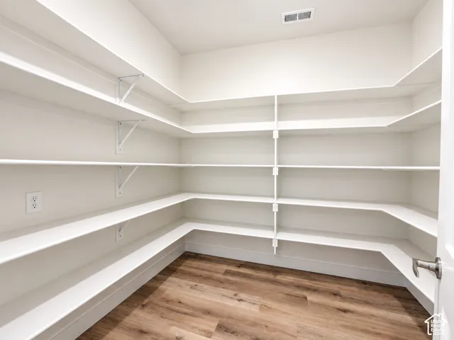 Walk-in storage area featuring wrap-around white shelving, wall-mounted electrical outlet, and wood-finish flooring