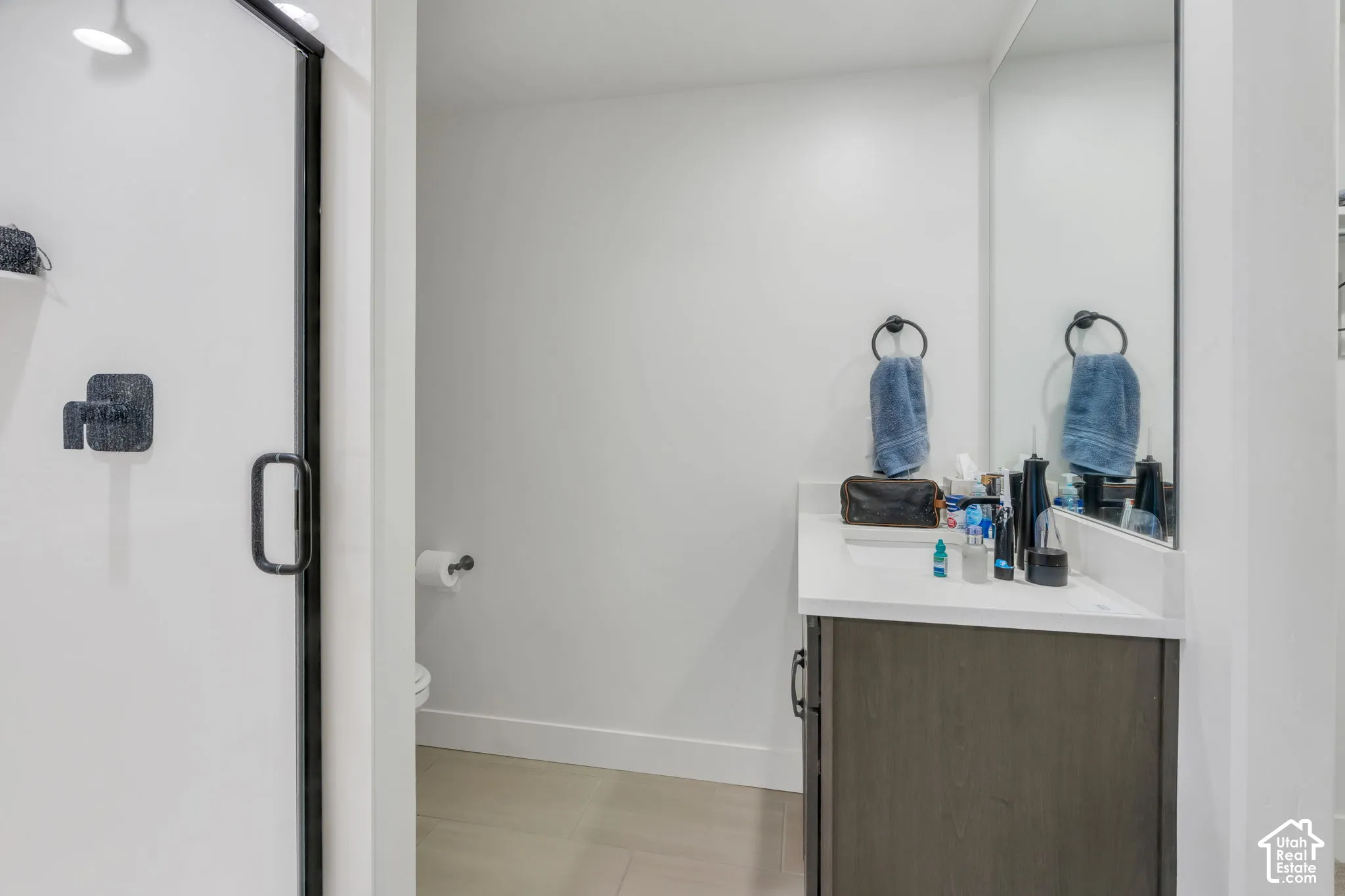 Bathroom featuring a vanity with a solid-surface countertop, full-width mirror, dark-toned cabinetry, and a walk-in shower with matte black hardware and a glass enclosure