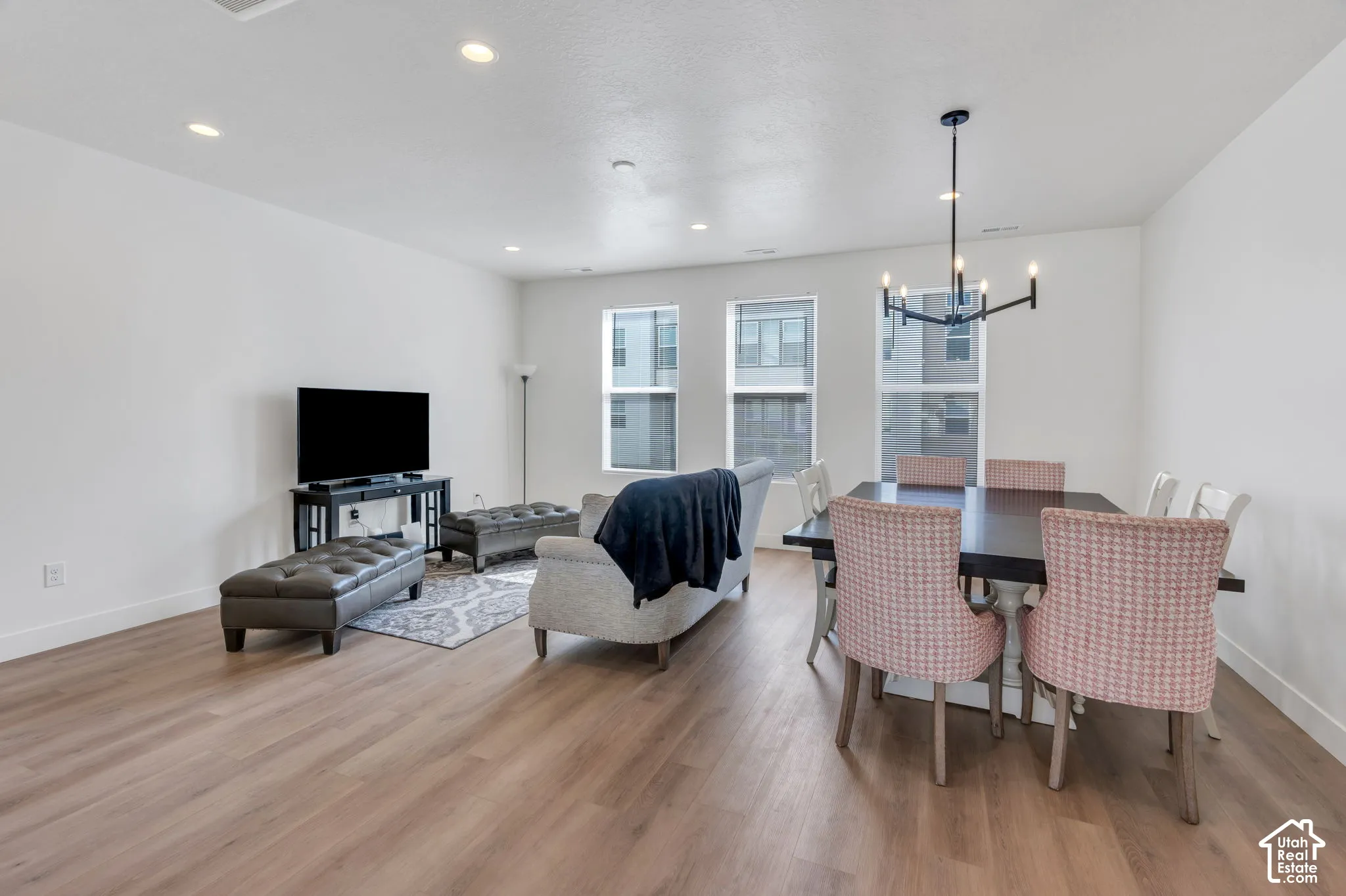 Open-concept room featuring wood-finish flooring, recessed lighting, expansive windows, and a modern multi-arm chandelier