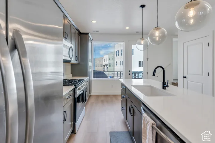 Kitchen featuring stainless steel appliances, quartz countertops, a central island with an undermount sink, dark-toned cabinetry, and wood-finish flooring
