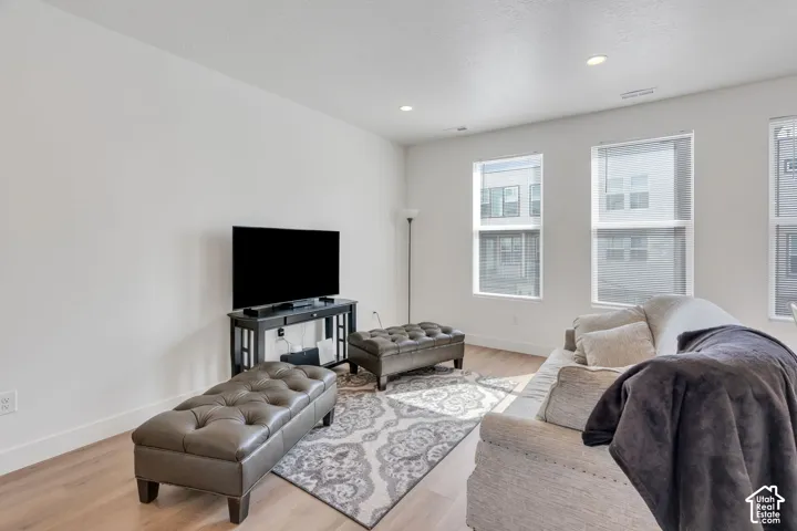 Living area featuring wood-finish flooring, neutral wall paint, and multiple large windows with integrated blinds, complemented by recessed ceiling lighting
