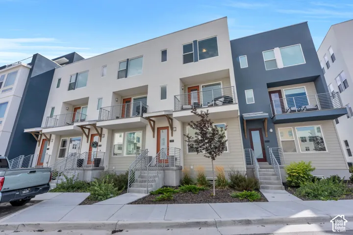 Modern multi-level exterior featuring a mix of stucco and horizontal siding, private balconies with metal railings, elevated entryways with concrete steps, and large windows