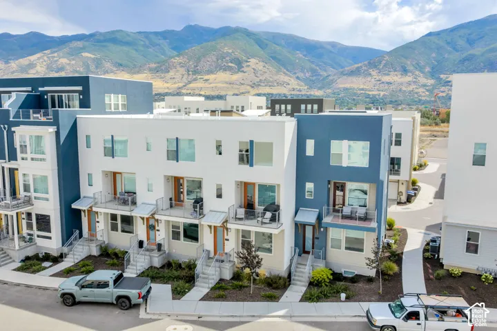 Contemporary multi-level townhome exteriors featuring dual-tone stucco facades, metal-accented awnings, glass-railing balconies, and mountain backdrops