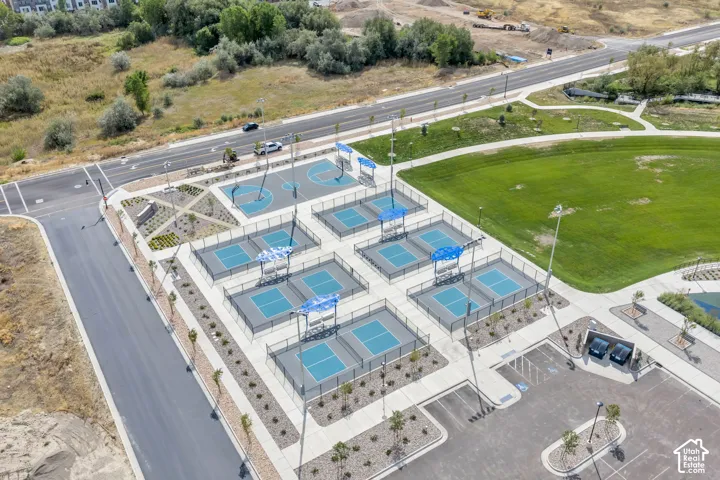 Recreational facility featuring multiple fenced pickleball courts, a basketball court, paved parking area, and manicured green space