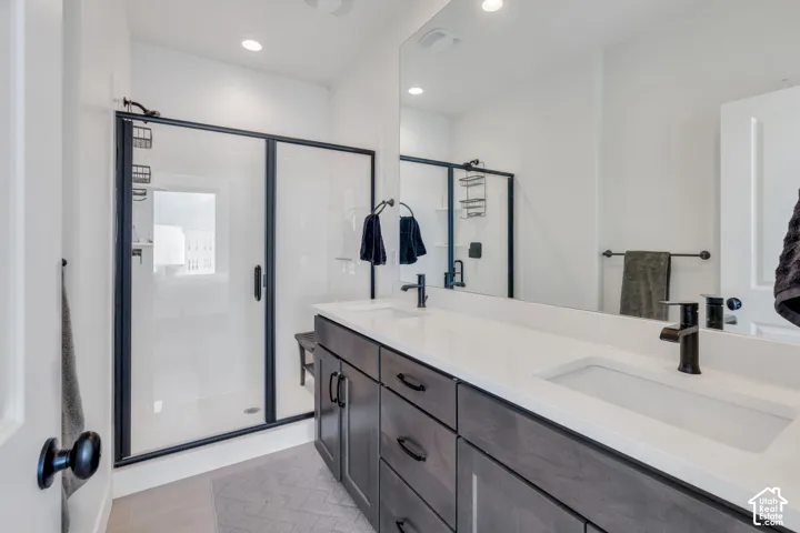 Double-sink vanity with matte black fixtures, quartz countertop, dark cabinetry, and a walk-in shower with a glass enclosure