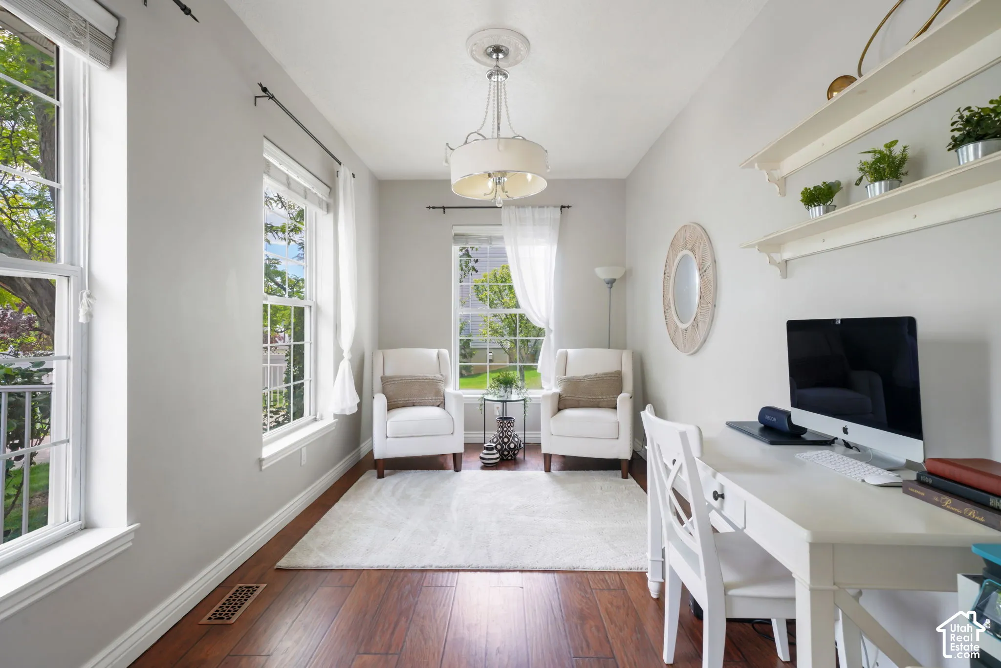 Room featuring wood-finish flooring, three windows with natural light, a drum-style pendant light with ceiling medallion, and white built-in wall shelving