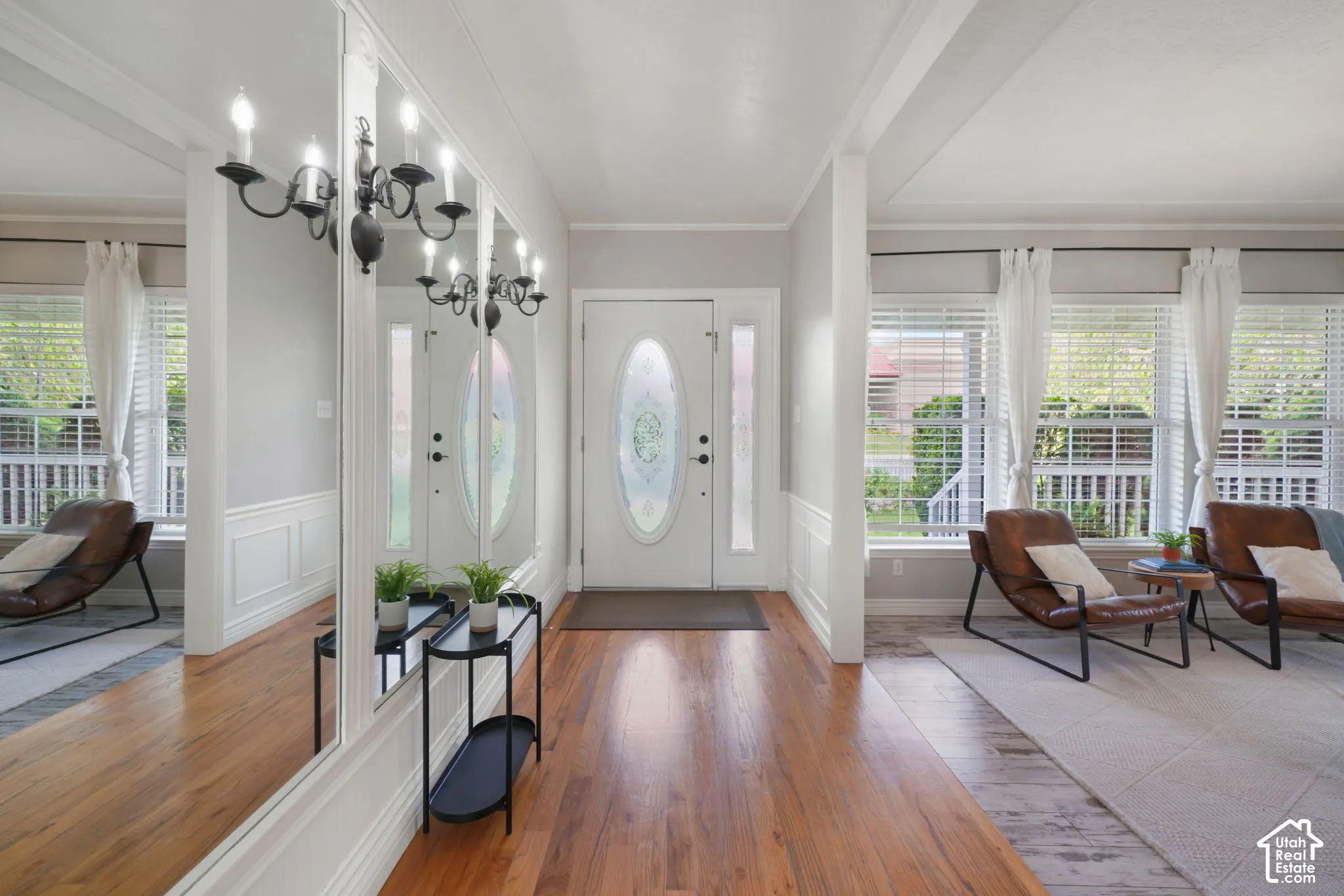 Foyer featuring wood-finish flooring, full-length wall mirror, ornate metal wall-mounted light fixture, white wainscoting, and an exterior door with decorative glass insert