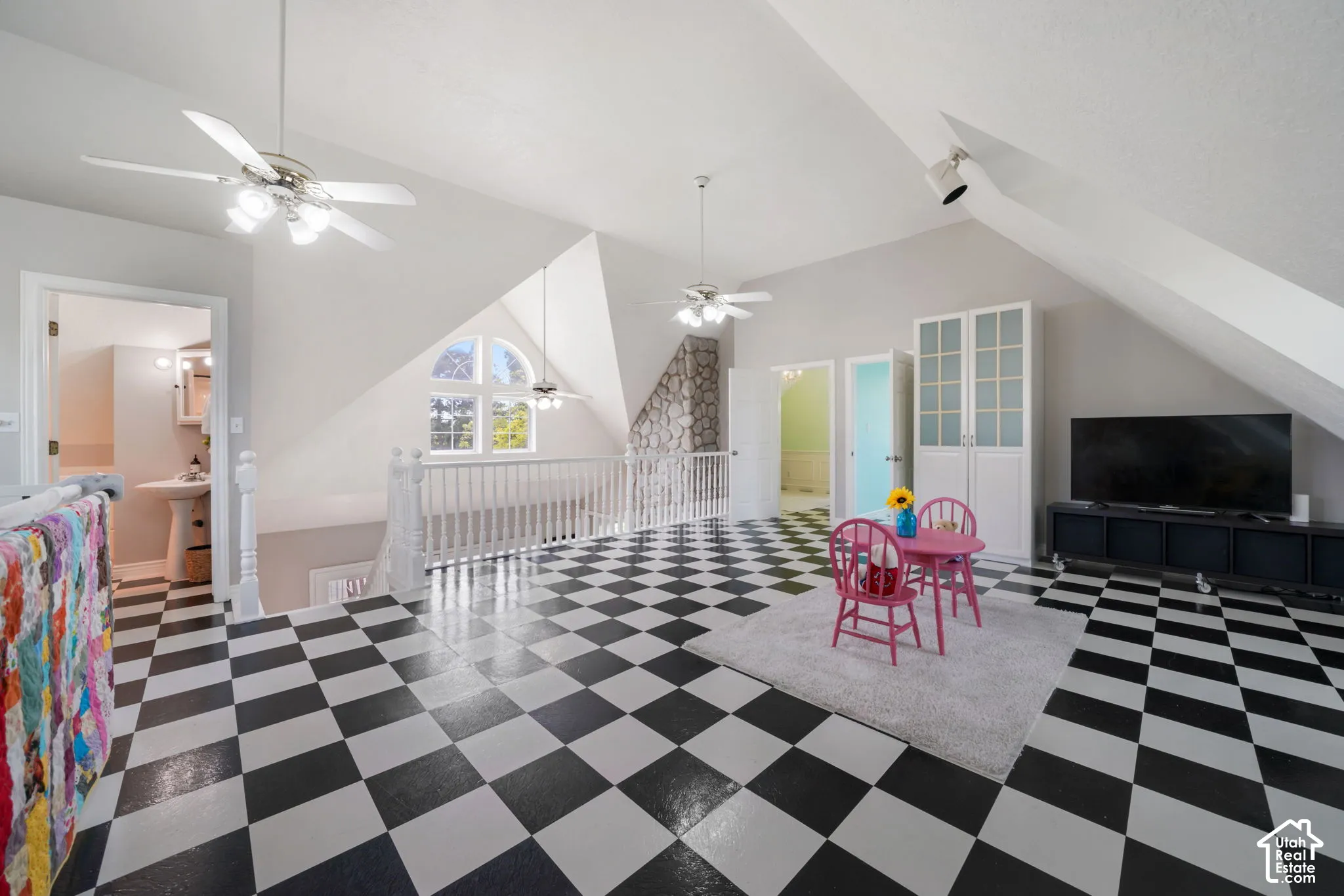 Vaulted ceilings featuring architectural dormers, stone-finished chimney breast, black and white checkered flooring, arched window, and dual ceiling fans
