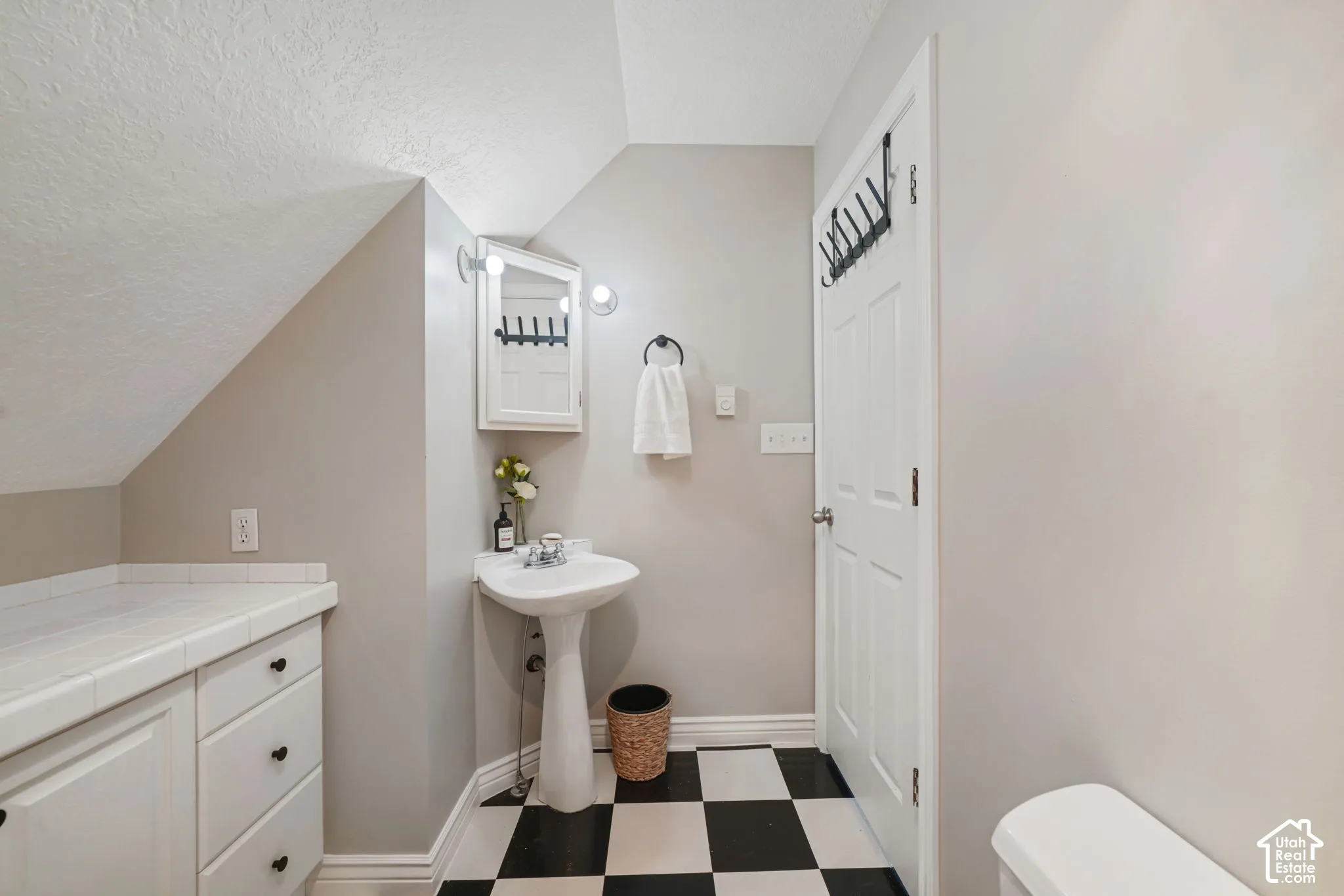Built-in cabinetry featuring tile countertops, white pedestal sink with chrome faucet, corner medicine cabinet with integrated lighting, and high-contrast checkered flooring