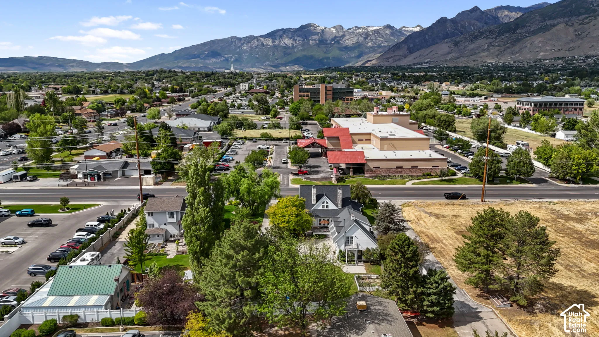 Aerial perspective featuring a multi-story residence with a gabled roofline, situated against a prominent mountain backdrop with mature perimeter trees and open acreage