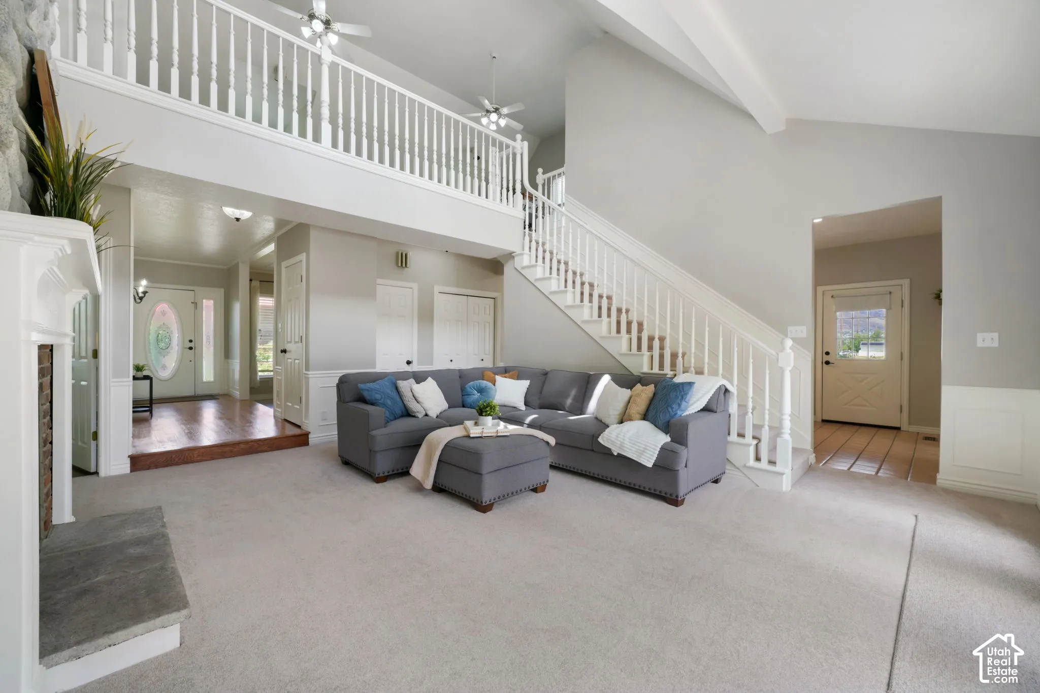 Two-story vaulted ceilings, fireplace with stone-finish surround, wooden staircase with decorative balustrade, wood-finish flooring, and crisp white wainscoting