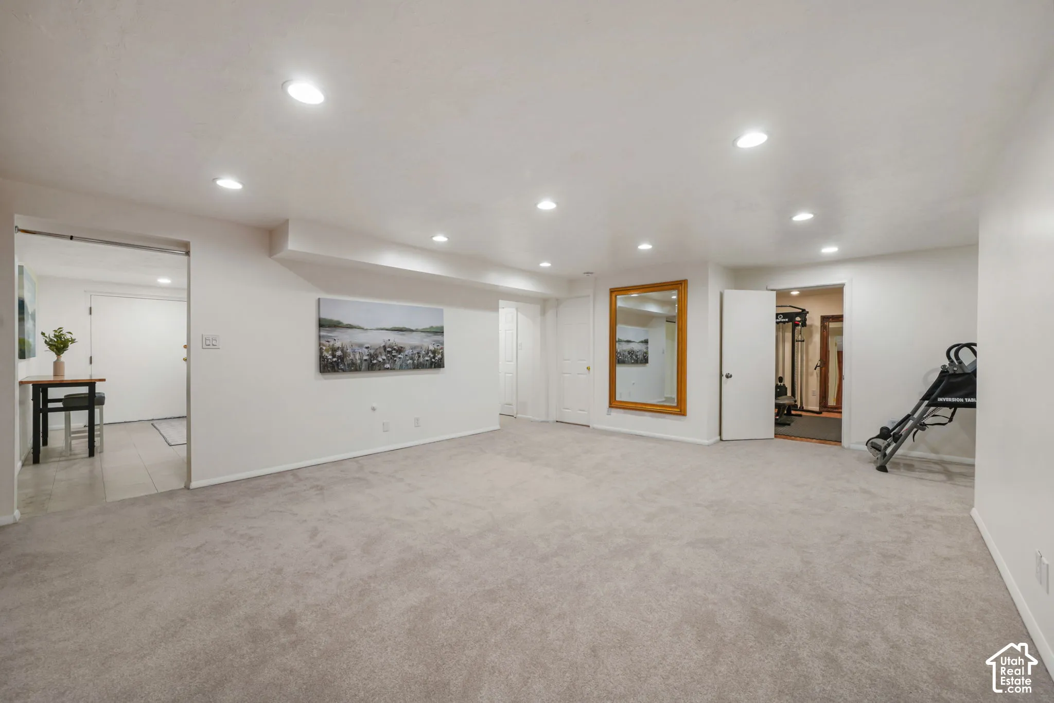 Expansive open-concept room featuring neutral wall-to-wall carpeting, recessed ceiling lighting, and a large wall-mounted mirror with a wood frame