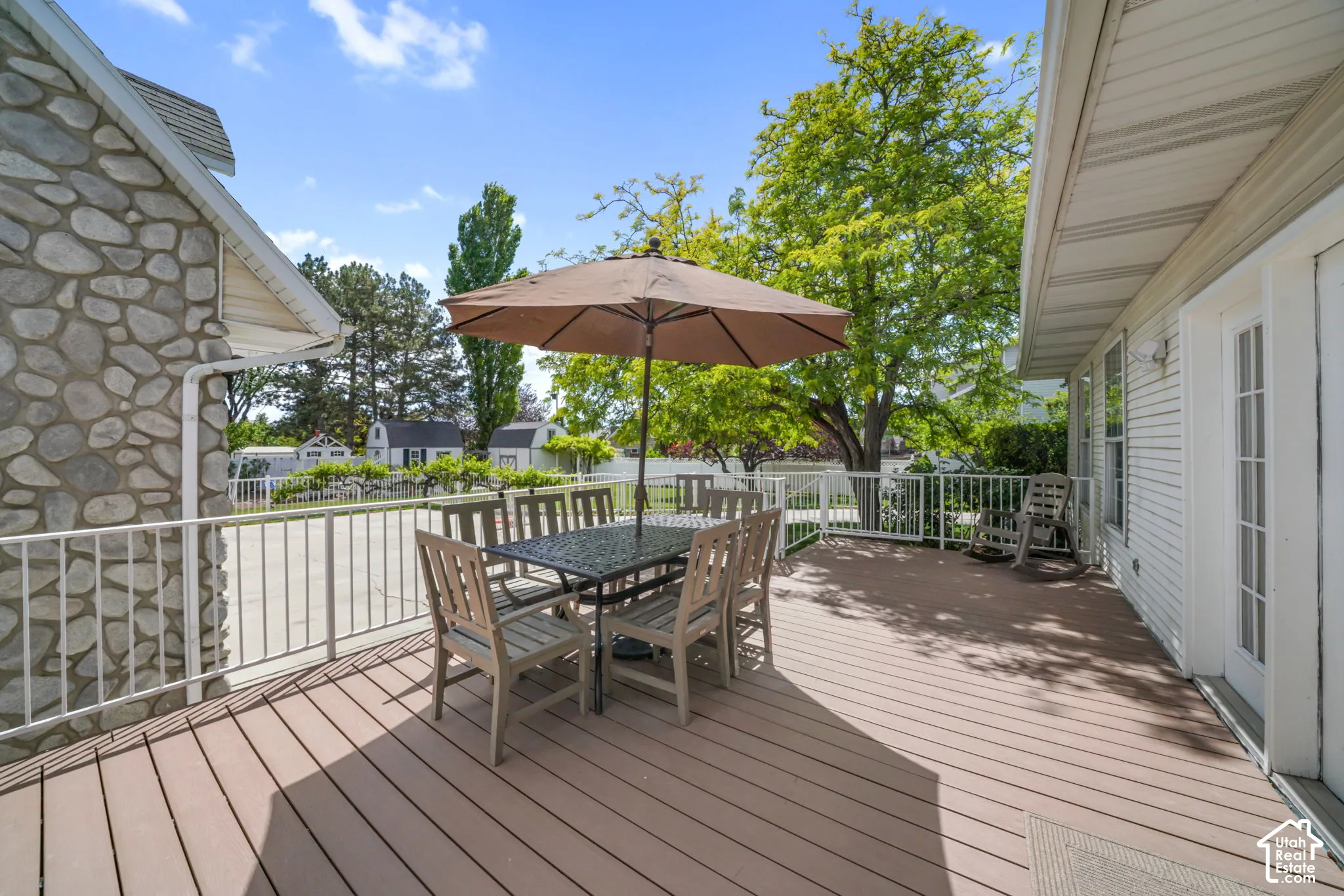 Elevated deck featuring composite decking, white metal railing, and stone exterior accent wall