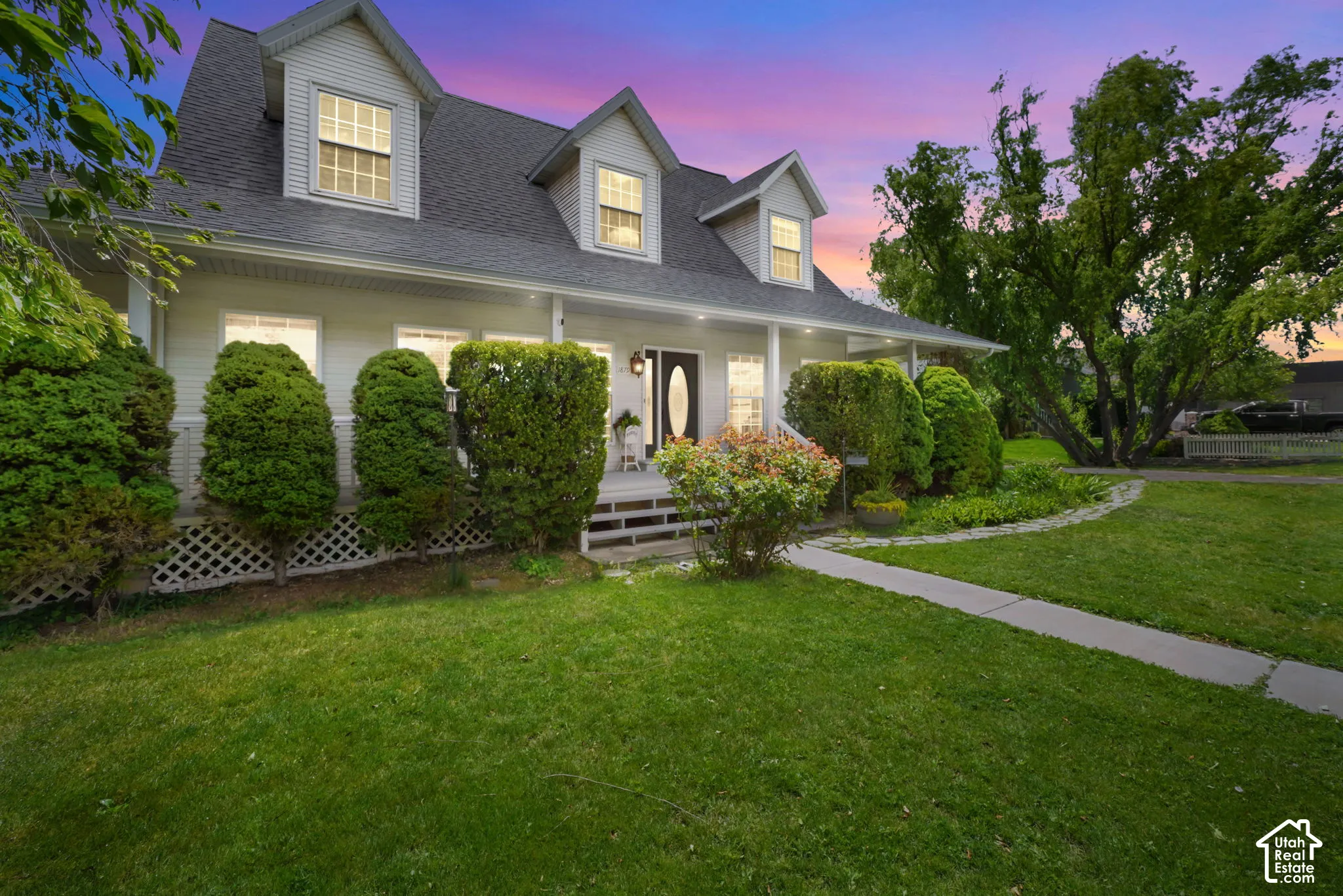 Two-story exterior featuring light-colored horizontal siding, a covered front porch, three dormer windows, and a lattice foundation skirt