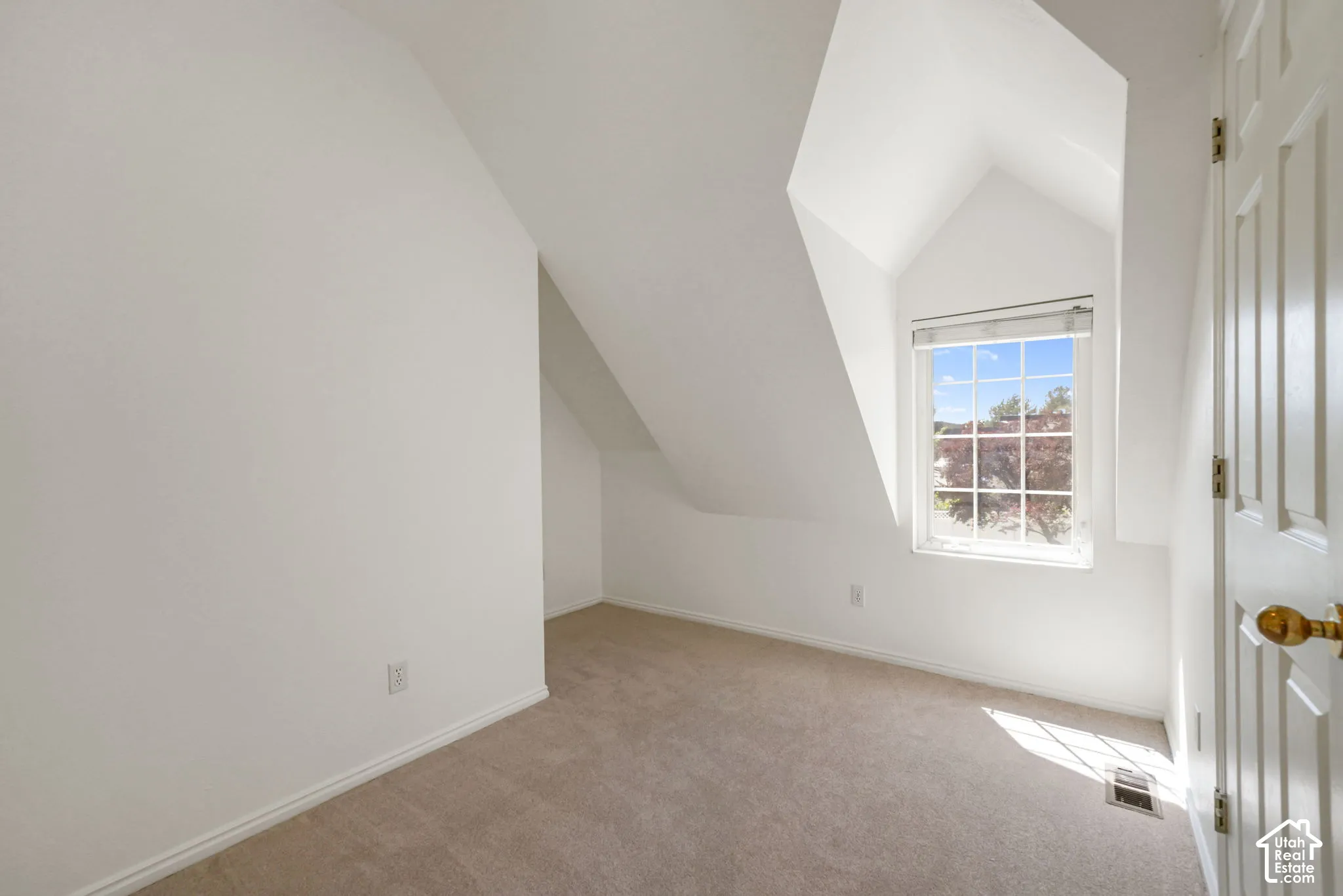 Room featuring vaulted ceilings, neutral carpeting, and a multi-pane window with a roller shade