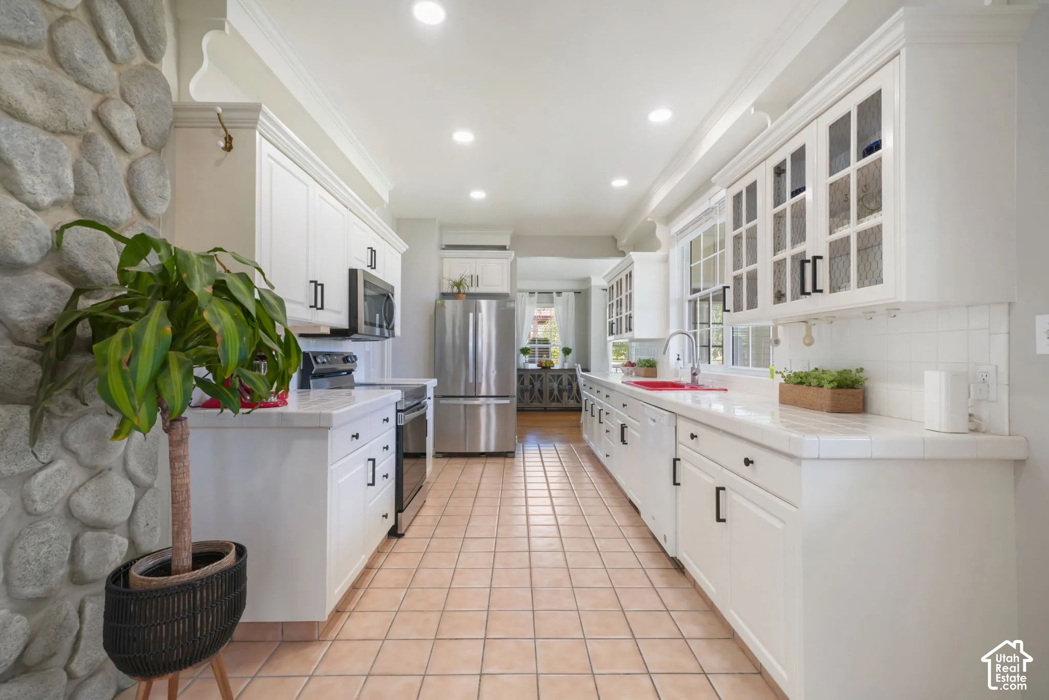 Kitchen featuring white cabinetry with glass-front uppers, tile countertops, stainless steel appliances, a stone-accented wall, and tile flooring