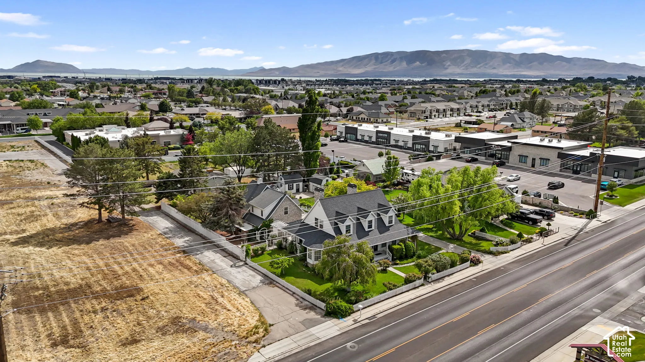 Aerial perspective featuring a multi-story residence with a gabled roof, dormer windows, wrap-around porch, and mature trees on a corner lot