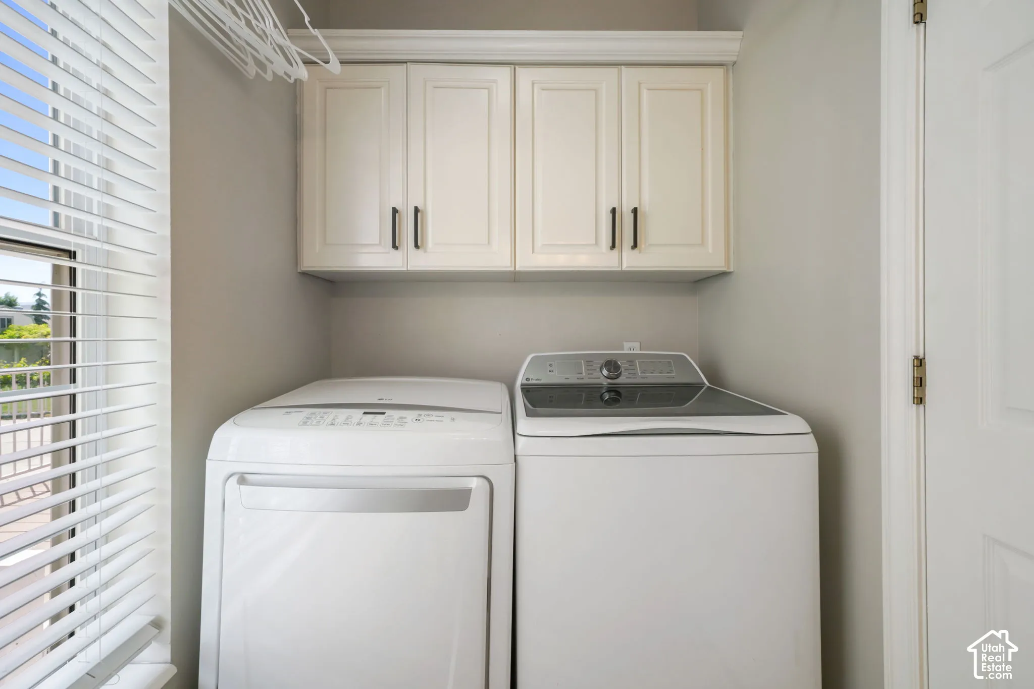 Laundry room featuring built-in cream cabinetry with crown molding, overhead storage, and horizontal slat window blinds