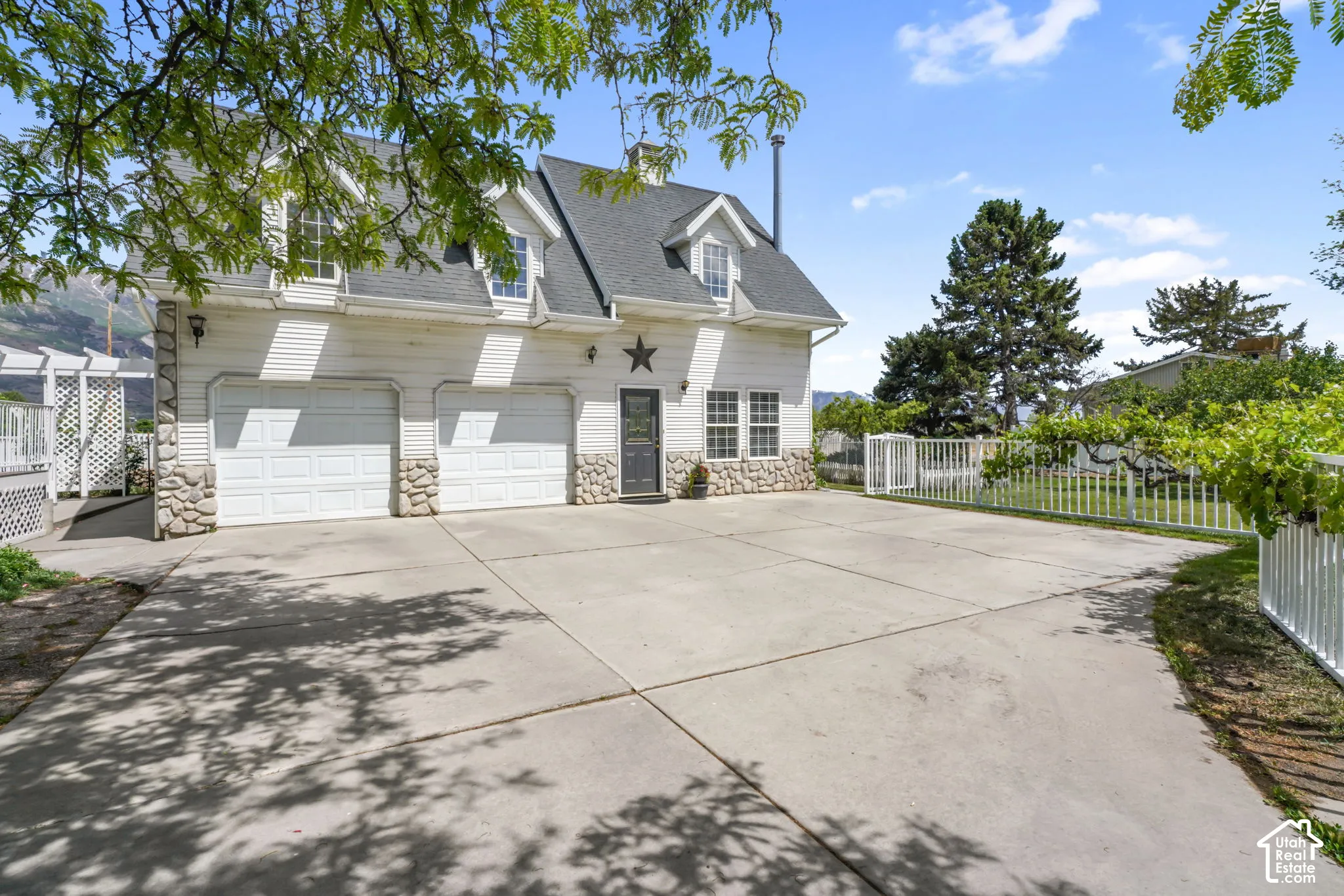 Two-story exterior featuring white horizontal siding, a stone veneer foundation, dormer windows, a dual-bay garage, and an expansive concrete driveway