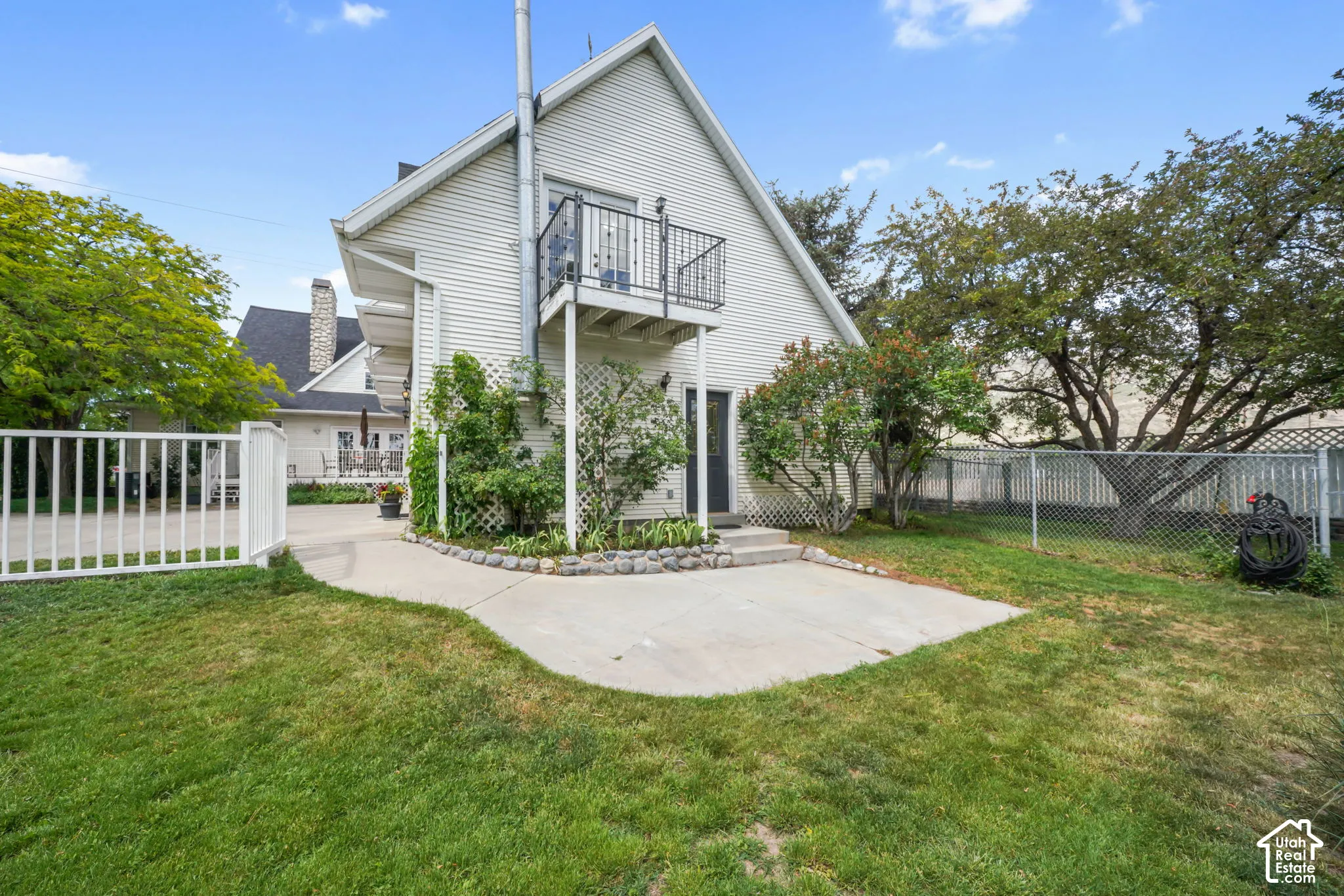 Exterior featuring horizontal siding, a second-story balcony with metal railing, a concrete patio, stone landscape edging, and white lattice accents