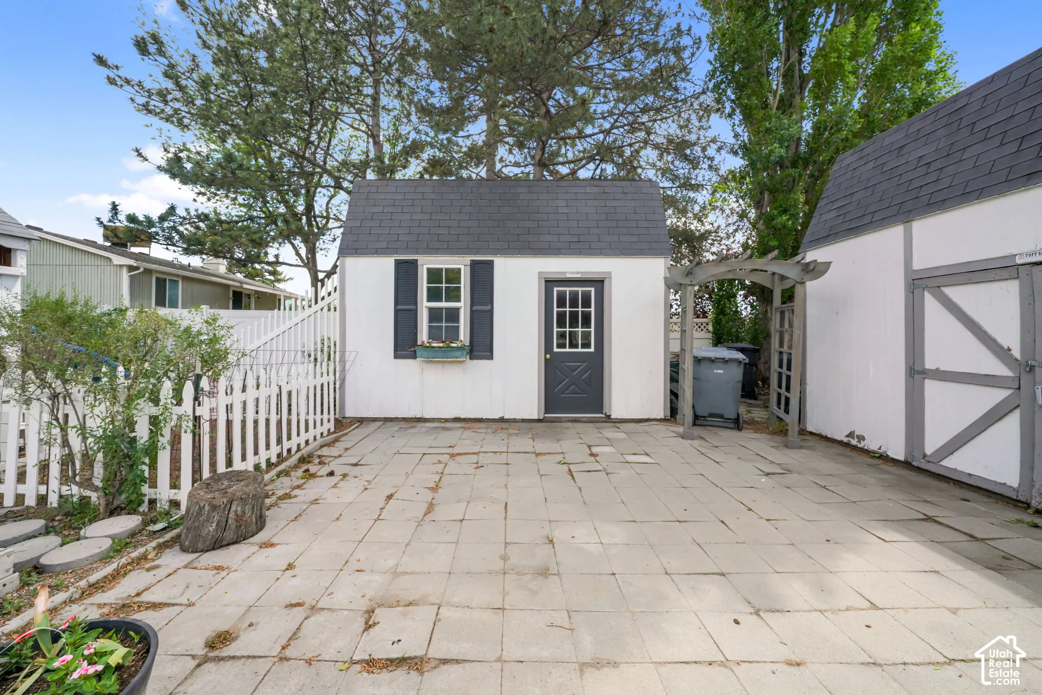 Detached storage structure featuring a gable roof, shingle siding, a multi-pane entry door, and decorative window shutters