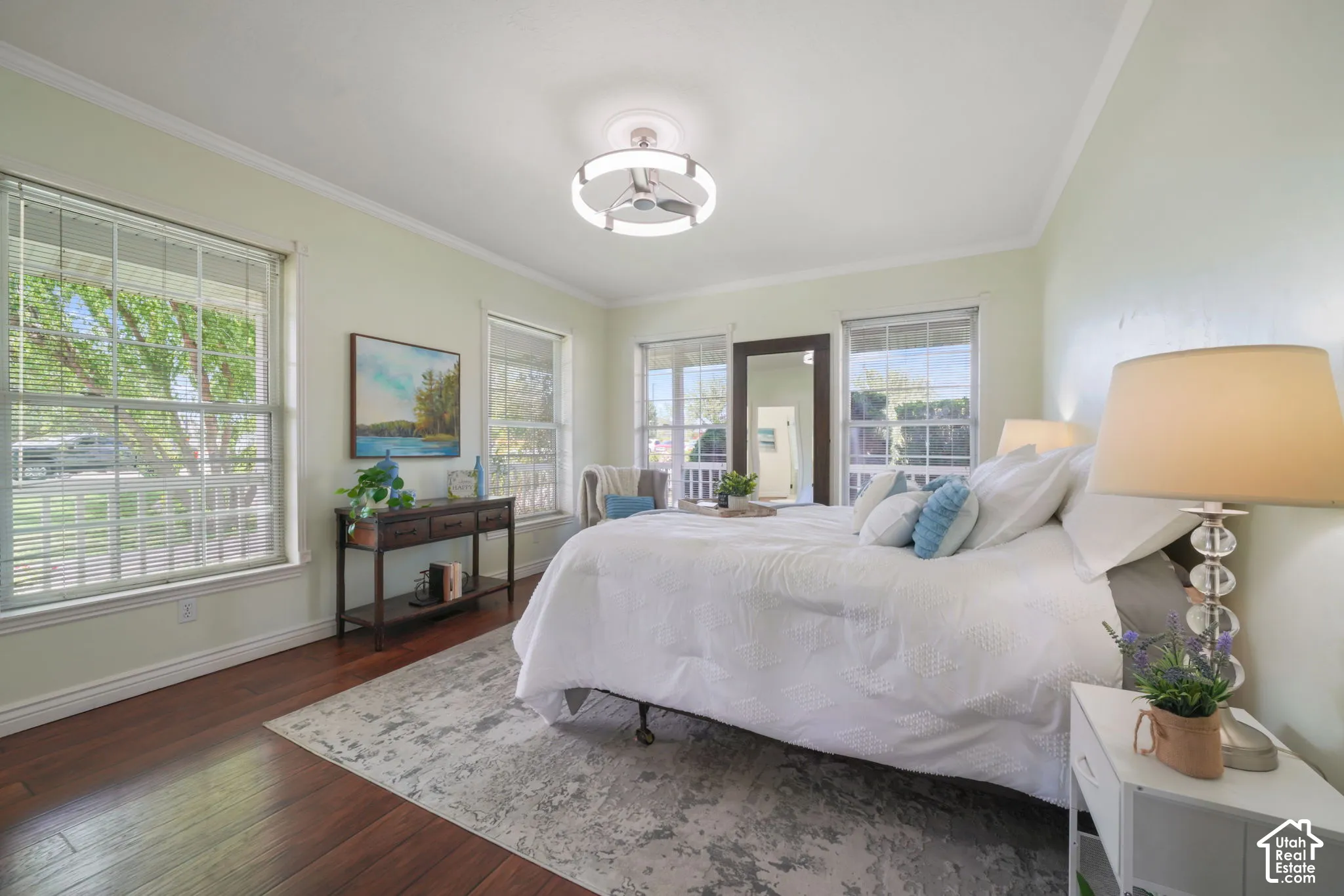 Room featuring wood-finish flooring, neutral wall paint, three large windows with blinds, and a circular LED flush-mount ceiling fixture