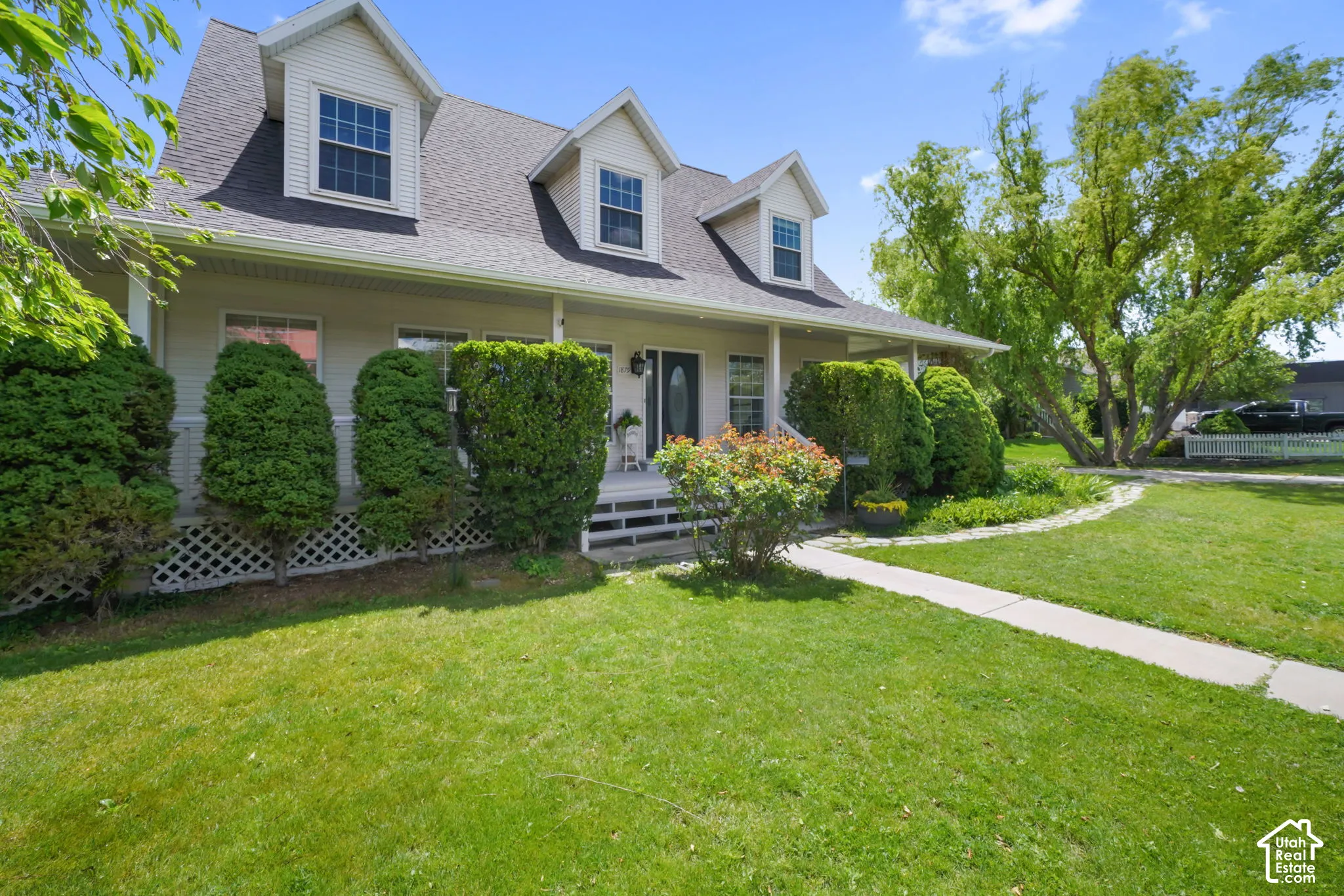 Two-story residence featuring light-toned horizontal siding, a covered front porch, three dormer windows, and a paved walkway