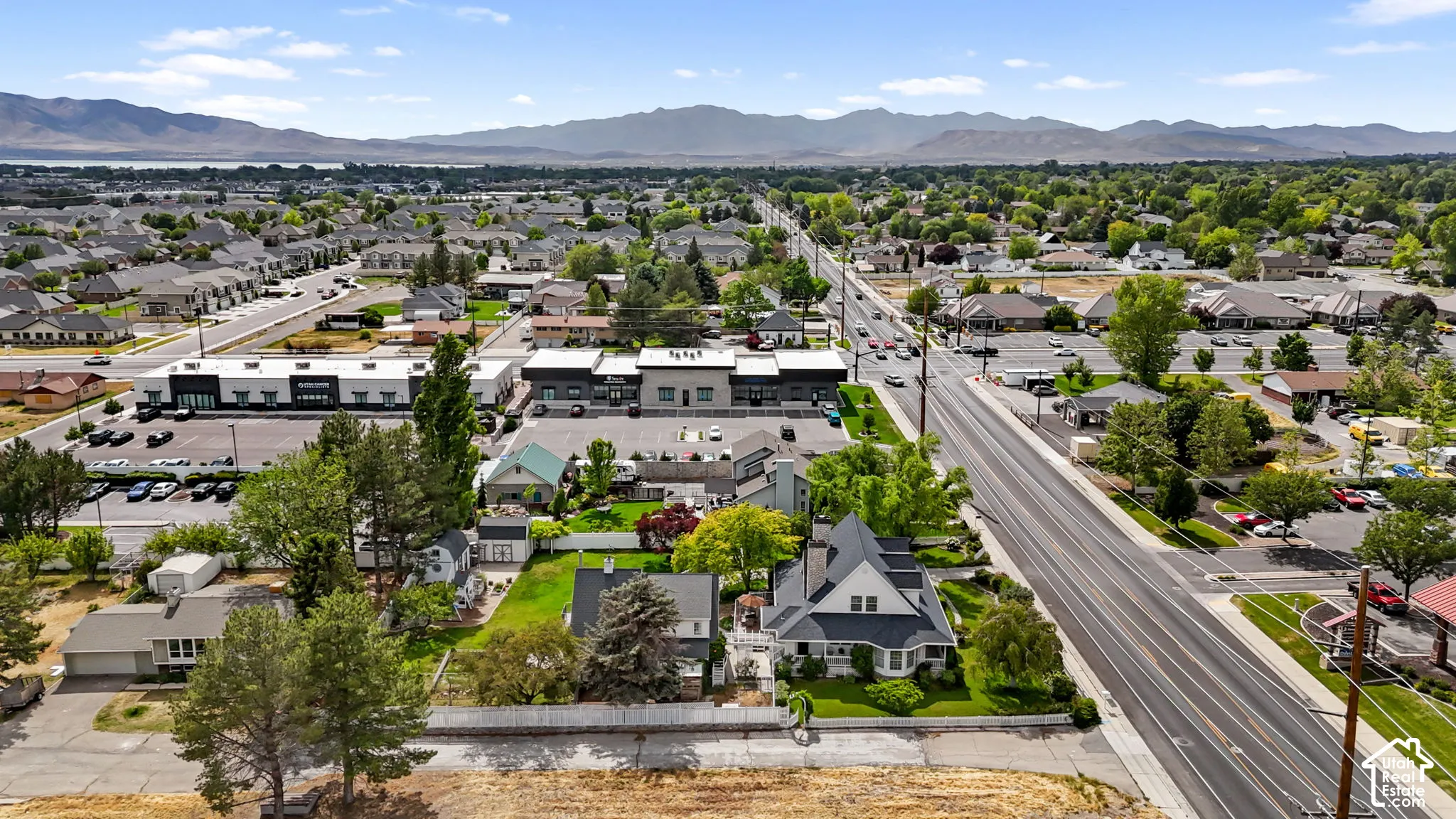 Aerial perspective of the property featuring a multi-story residence with a pitched roof, prominent chimneys, mature trees, and a fenced perimeter