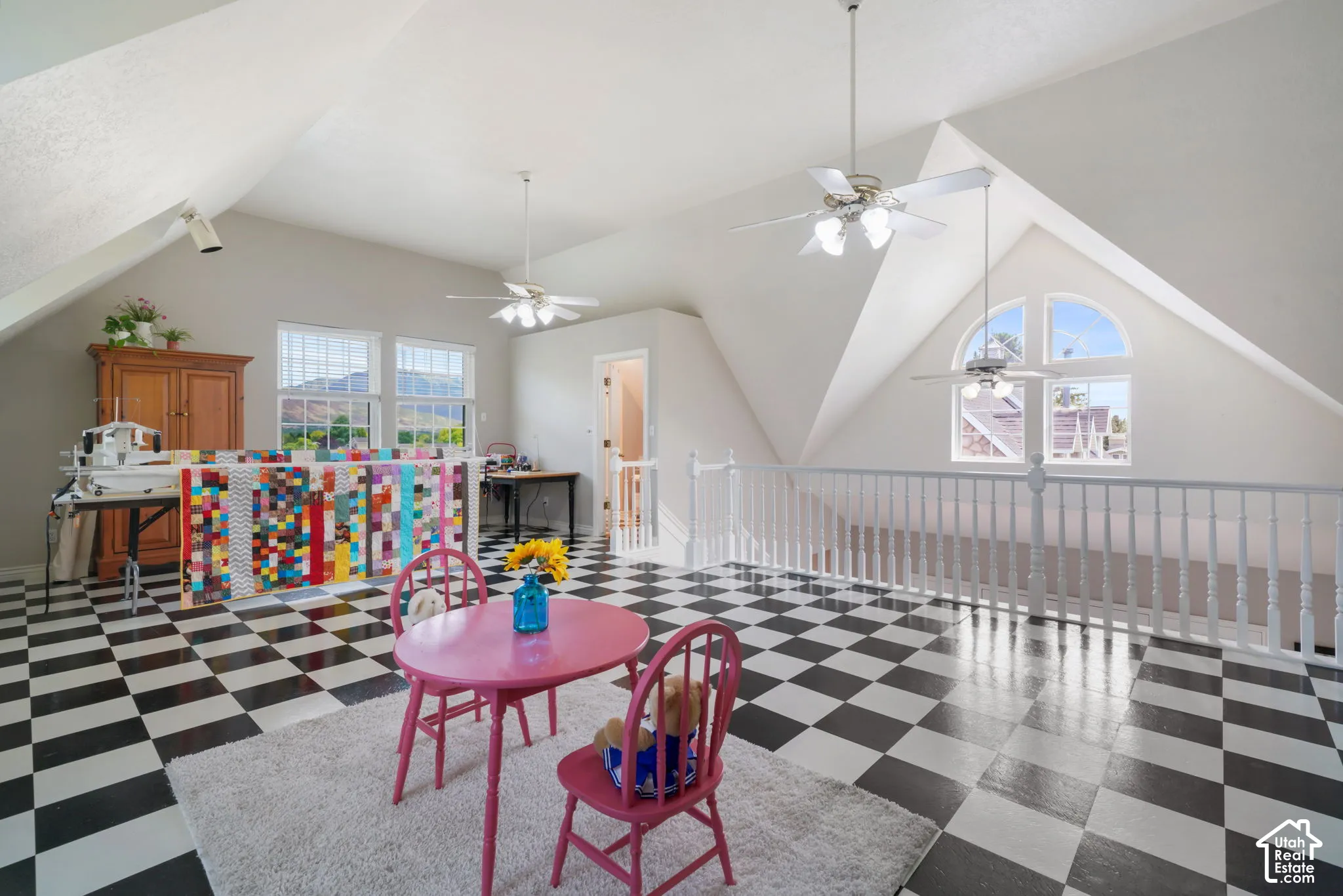 Open-concept area featuring vaulted ceilings, checkered pattern flooring, white wooden balustrade, multiple ceiling fans, and an arched window