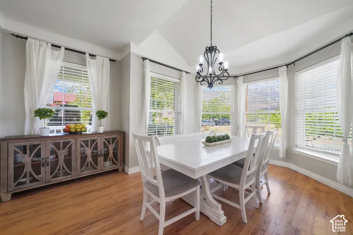 Dining area featuring vaulted ceilings, wood-finish flooring, a bay window configuration, and a multi-arm chandelier