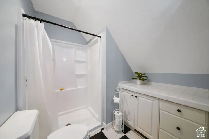 Bathroom featuring a shower stall with built-in shelving, white cabinetry with a tiled countertop, and black-and-white checkered flooring