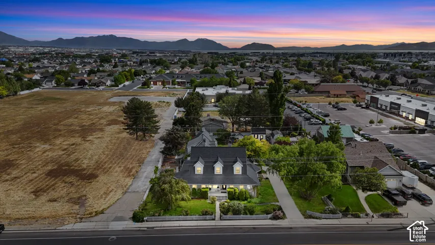 Aerial perspective of a multi-story residence featuring a shingled roof, three gabled dormers, a covered front porch, and mature trees, set against a mountain backdrop
