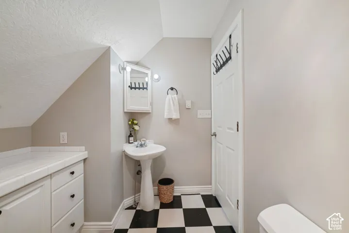 Built-in cabinetry featuring tile countertops, white pedestal sink with chrome faucet, corner medicine cabinet with integrated lighting, and high-contrast checkered flooring