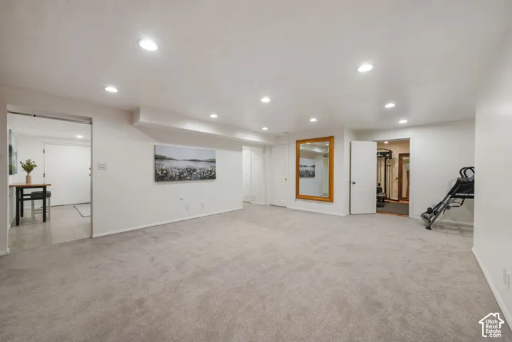 Expansive open-concept room featuring neutral wall-to-wall carpeting, recessed ceiling lighting, and a large wall-mounted mirror with a wood frame