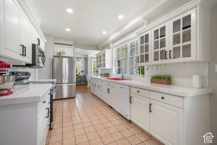Kitchen featuring white cabinetry with glass-front uppers, tiled countertops, stainless steel appliances, and ceramic tile flooring