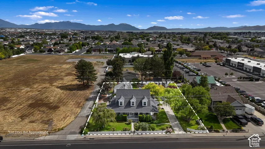 Two-story residence with a gabled roof, three dormer windows, a wrap-around porch, and extensive mature landscaping, set against a mountainous horizon