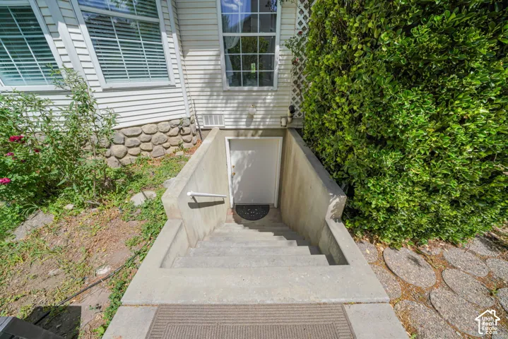 Exterior stairwell entrance with concrete retaining walls, white steel door, and metal handrail, finished with horizontal siding and stone foundation detail