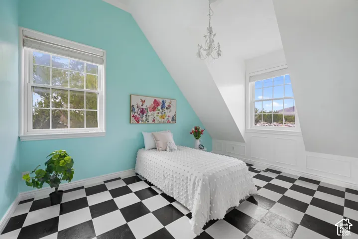Room featuring vaulted ceilings, checkered pattern flooring, two double-hung windows, decorative wall molding, and a traditional chandelier