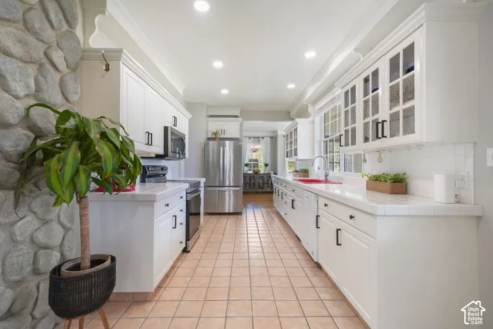Kitchen featuring white cabinetry with glass-front uppers, tile countertops, stainless steel appliances, a stone-accented wall, and tile flooring
