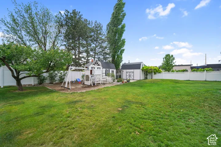 Expansive backyard featuring a manicured lawn, white vinyl fencing, two detached storage structures, and mature trees