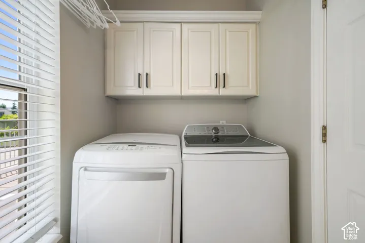 Laundry room featuring built-in cream cabinetry with crown molding, overhead storage, and horizontal slat window blinds