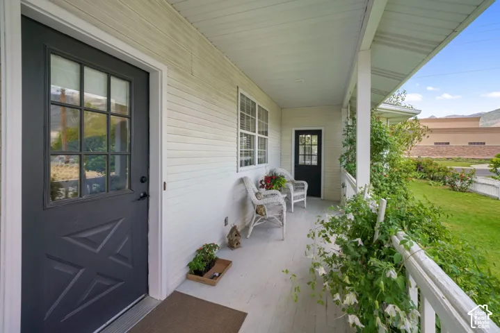 Covered front porch featuring white siding, dual dark-finished exterior doors with window panes, and painted wood-finish decking